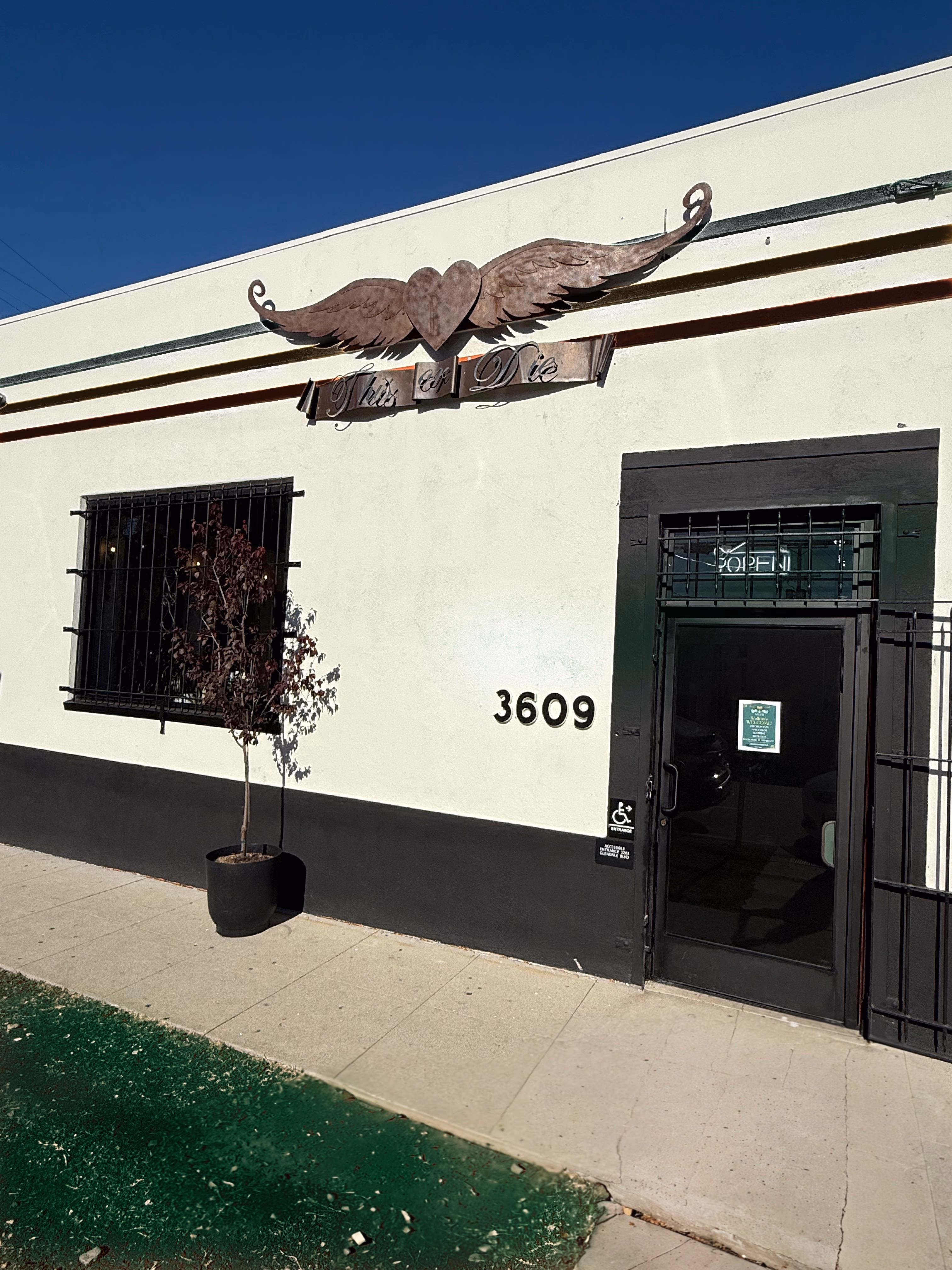 The front of This Or Die Salon at 3609 Edenhurst Ave — black door, carved winged-heart sign above it.