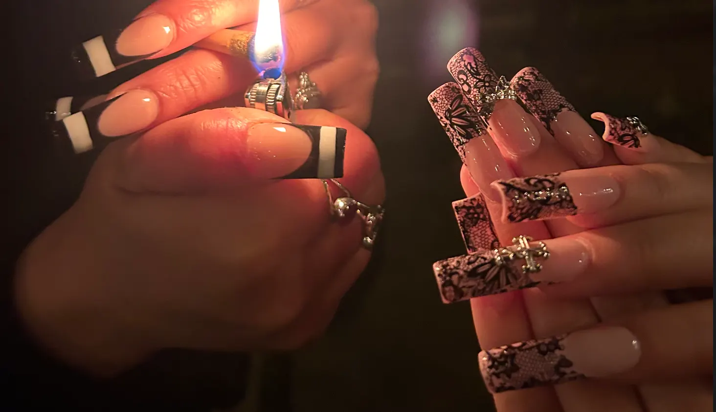 Violet's nails: a black and white French set held to a lighter flame on the left, and a long pink lace set with silver charms on the right