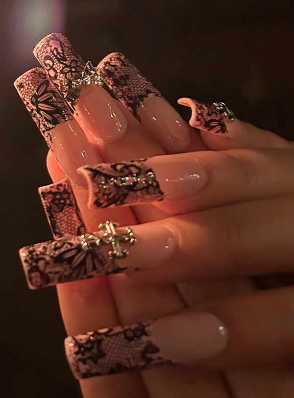 A long pink set by Violet with black lace nail art and silver charms.